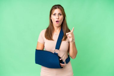 Middle age with broken arm and wearing a sling over isolated background intending to realizes the solution while lifting a finger up