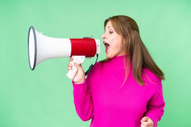 Middle age woman over isolated background shouting through a megaphone to announce something in lateral position