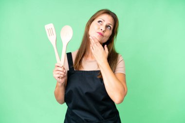 Middle age caucasian woman holding a rolling pin over isolated background looking up while smiling