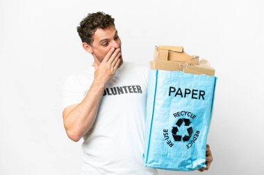 Brazilian man holding a recycling bag full of paper to recycle over isolated white background with surprise and shocked facial expression