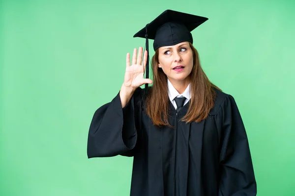 Middle age university graduate woman over isolated background listening to something by putting hand on the ear