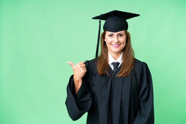Middle age university graduate woman over isolated background pointing to the side to present a product
