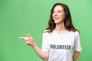 İzole edilmiş arka planda genç gönüllü beyaz kadın parmak göstererek bir ürün sunuyor.