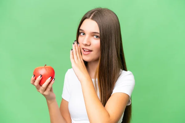 Teenager caucasian girl holding an apple over isolated background whispering something