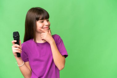 Küçük şarkıcı kız izole edilmiş bir arka planda mikrofonu eline alıp bir fikir üretiyor ve ona bakıyor.