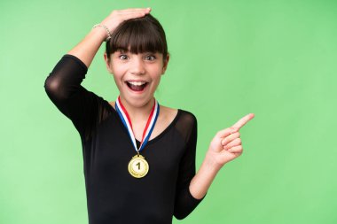 Tecrit edilmiş arka planda madalyaları olan küçük beyaz kız şaşırdı ve parmağını yana uzattı.