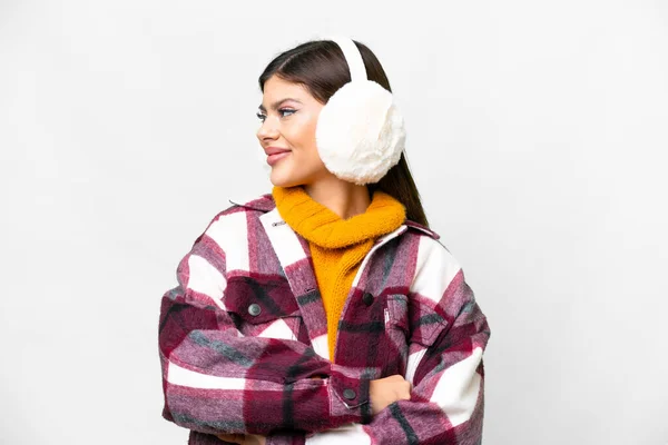 Young Russian woman wearing winter muffs over isolated white background looking side