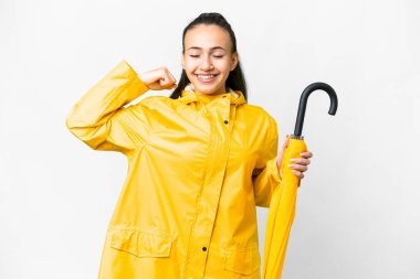Yağmura dayanıklı ceketi ve şemsiyesi olan genç bir Arap kadın izole edilmiş beyaz arka planda güçlü bir jest yapıyor.