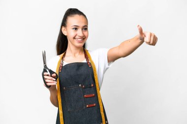 İzole edilmiş beyaz arka planda genç bir terzi kadın baş parmak hareketi yapıyor.