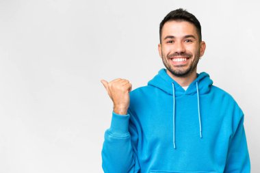 İzole edilmiş beyaz arka planı olan yakışıklı beyaz bir adam bir ürün sunmak için kenarı işaret ediyor.