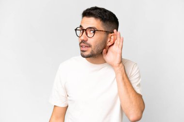 İzole edilmiş beyaz arka planda genç, yakışıklı beyaz bir adam elini kulağına koyarak bir şeyler dinliyor.