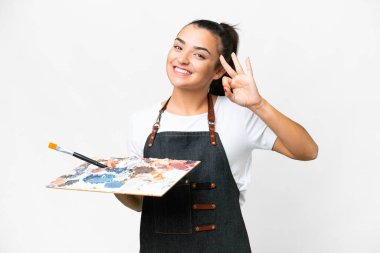 İzole edilmiş beyaz arkaplan üzerinde palet tutan genç sanatçı kadın parmaklarıyla tamam işareti gösteriyor.