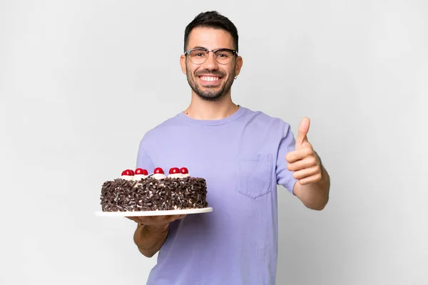 若いですCaucasian男保持誕生日ケーキ隔離上の白い背景とともに親指アップ何か良いことが起こったので — ストック写真