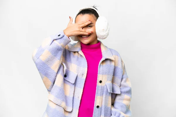 Young woman wearing winter muffs over isolated white background covering eyes by hands and smiling