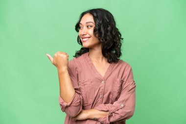 Arjantinli genç bir kadın izole edilmiş arka planda bir ürün sunmak için kenarı işaret ediyor.