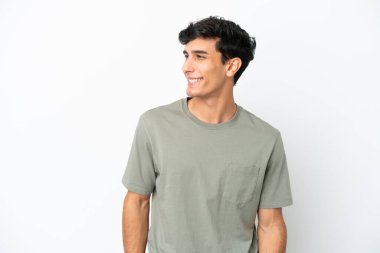 Arjantinli genç bir adam beyaz arka planda izole edilmiş, yana bakıyor ve gülümsüyor.