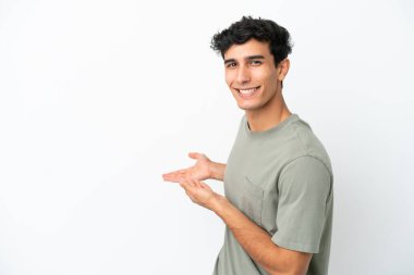 Arjantinli genç adam beyaz arka planda izole edilmiş. Davet etmek için ellerini yana uzatıyor.