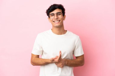 Arjantinli genç adam pembe arka planda yalnız gülüyor.