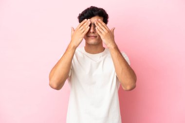 Arjantinli genç adam pembe arka planda izole edilmiş gözleri elleriyle kaplayan