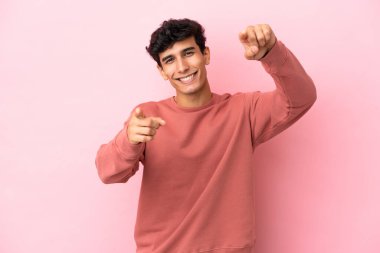 Arjantinli genç bir adam pembe arka planda izole edilmiş mutlu bir ifadeyle ön tarafı işaret ediyor