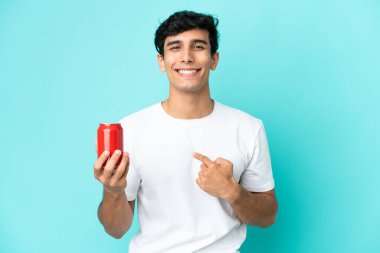 Arjantinli genç bir adam mavi arka planda izole edilmiş bir içecek tutuyor. Şaşırtıcı yüz ifadesi var.