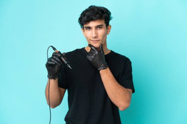 Dövme sanatçısı Arjantinli adam mavi arka planda izole edilmiş düşünüyor