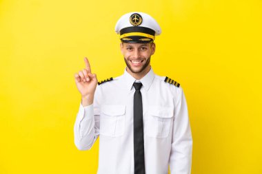 Kafkasyalı uçak pilotu sarı arka planda izole edildi ve en iyinin işareti olarak parmağını kaldırdı.