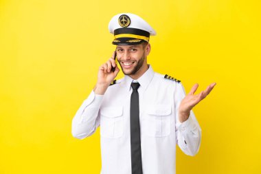 Kafkasyalı pilot sarı arka planda izole edilmiş bir şekilde cep telefonuyla sohbet ediyor.