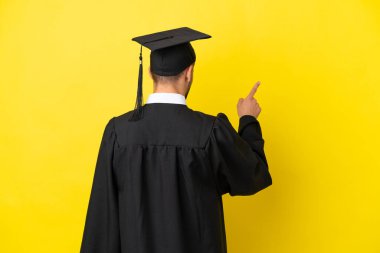 Genç üniversite mezunu, sarı arka planda izole edilmiş beyaz bir adam işaret parmağıyla işaret ediyor.
