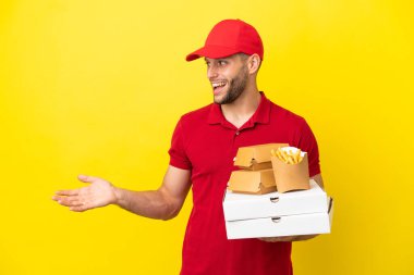 Pizza teslimatçısı pizza kutularını ve hamburgerleri alıp arka planda sürpriz bir ifadeyle yan tarafa bakıyor.