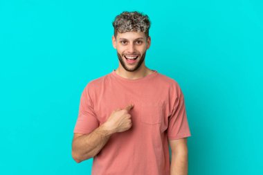 Mavi arka planda mahsur kalmış yakışıklı, beyaz bir adam. Şaşırtıcı bir yüz ifadesi var.