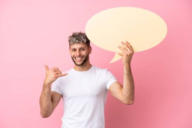 Pembe arka planda izole edilmiş yakışıklı beyaz bir adam boş bir konuşma balonu tutuyor ve telefon jesti yapıyor.