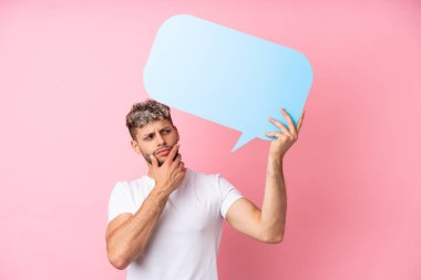 Pembe arka planda izole edilmiş yakışıklı beyaz adam boş bir konuşma balonu tutuyor ve düşünüyor.