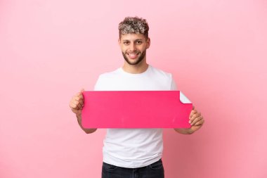 Pembe arka planda izole edilmiş yakışıklı beyaz bir adam elinde boş bir levha tutuyor.