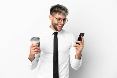 Beyaz arka planda izole edilmiş beyaz bir iş adamı elinde kahve ve bir cep telefonu tutuyor.