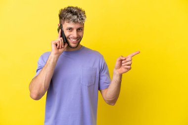 Sarı arka planda izole edilmiş cep telefonu kullanan genç, beyaz bir adam.
