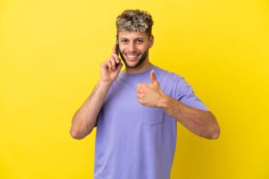Sarı arka planda izole edilmiş cep telefonu kullanan beyaz bir adam işaret veriyor.
