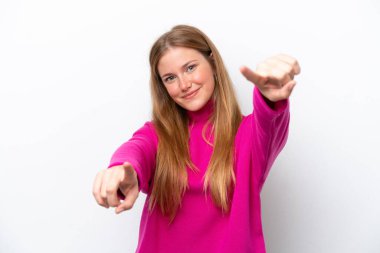 Beyaz arka planda izole genç beyaz kadın mutlu bir ifadeyle ön tarafı işaret ediyor.