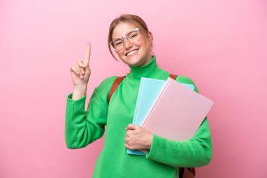 Pembe arka planda izole edilmiş genç beyaz kadın en iyinin işareti olarak parmağını kaldırıyor.