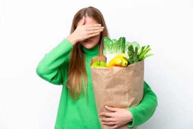 Beyaz arka planda izole edilmiş bir alışveriş torbası tutan beyaz bir kadın elleriyle gözlerini kapatıyor. Bir şey görmek istemiyorum.