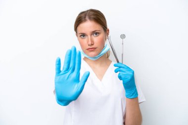 Beyaz arka planda izole edilmiş aletler taşıyan beyaz dişçi kadın dur hareketi yapıyor