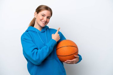Basketbol oynayan beyaz arka planda izole genç beyaz kadın bir ürünü sunmak için kenarı işaret ediyor.