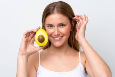 Beyaz arka planda izole edilmiş beyaz bir kadın elinde bir avokado tutarken gülümsüyor. Portreyi kapat