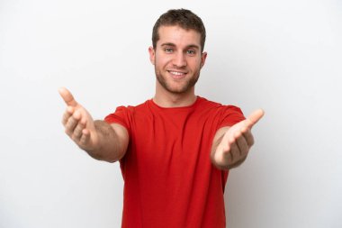 Beyaz arka planda izole edilmiş genç beyaz bir adam sunar ve davet eder.
