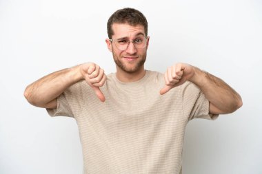 Beyaz arka planda izole edilmiş genç beyaz bir adam baş parmağını iki eliyle aşağı gösteriyor.