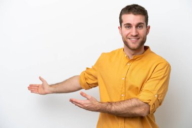 Beyaz arka planda soyutlanmış beyaz tenli genç adam davet edilmek için ellerini yana uzatıyor.