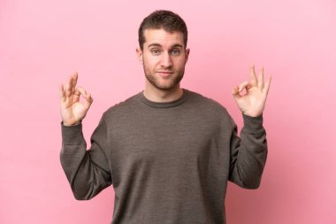 Zen pozisyonunda pembe arka planda izole edilmiş genç beyaz bir adam.