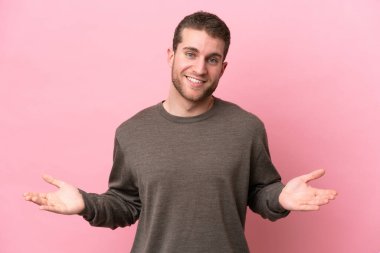 Pembe arka planda izole edilmiş genç beyaz adam mutlu ve gülümsüyor.