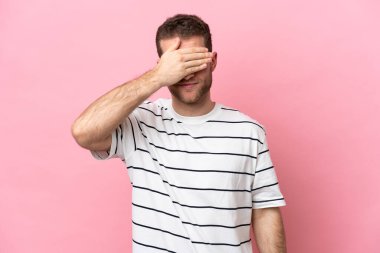Pembe arka planda izole edilmiş genç, beyaz bir adam gözlerini elleriyle kapatıyor. Bir şey görmek istemiyorum.