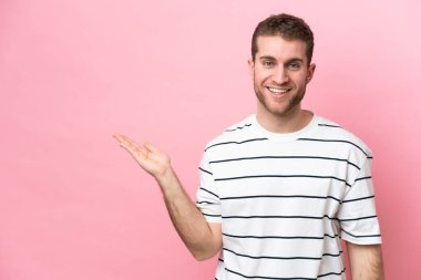 Pembe arka planda izole edilmiş genç beyaz bir adam bir ilan vermek için avucunun içinde hayali bir fotokopi makinesi tutuyor.